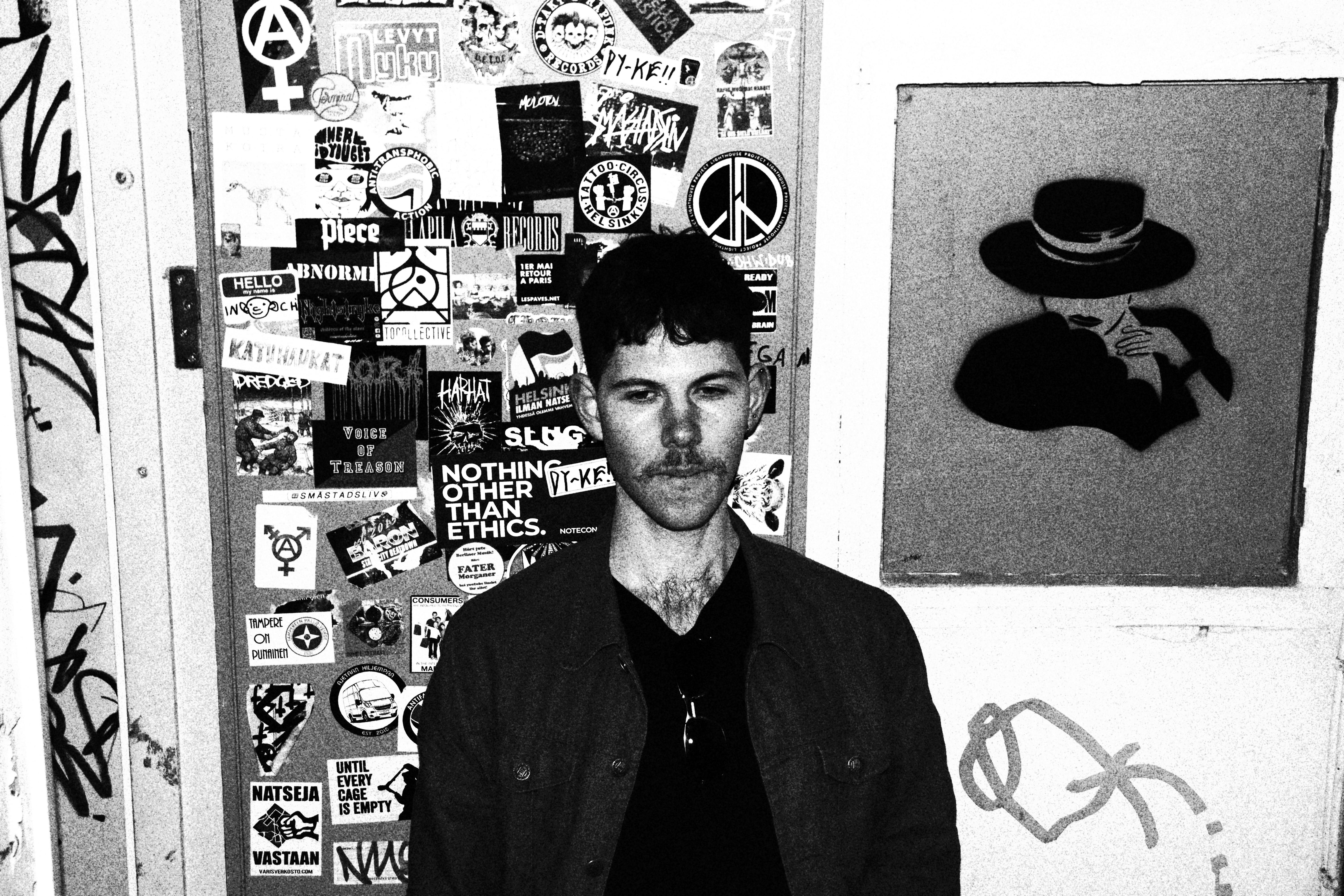 Black and white photograph of Twilight Courier against
            against a wall with stickers and grafitti on it