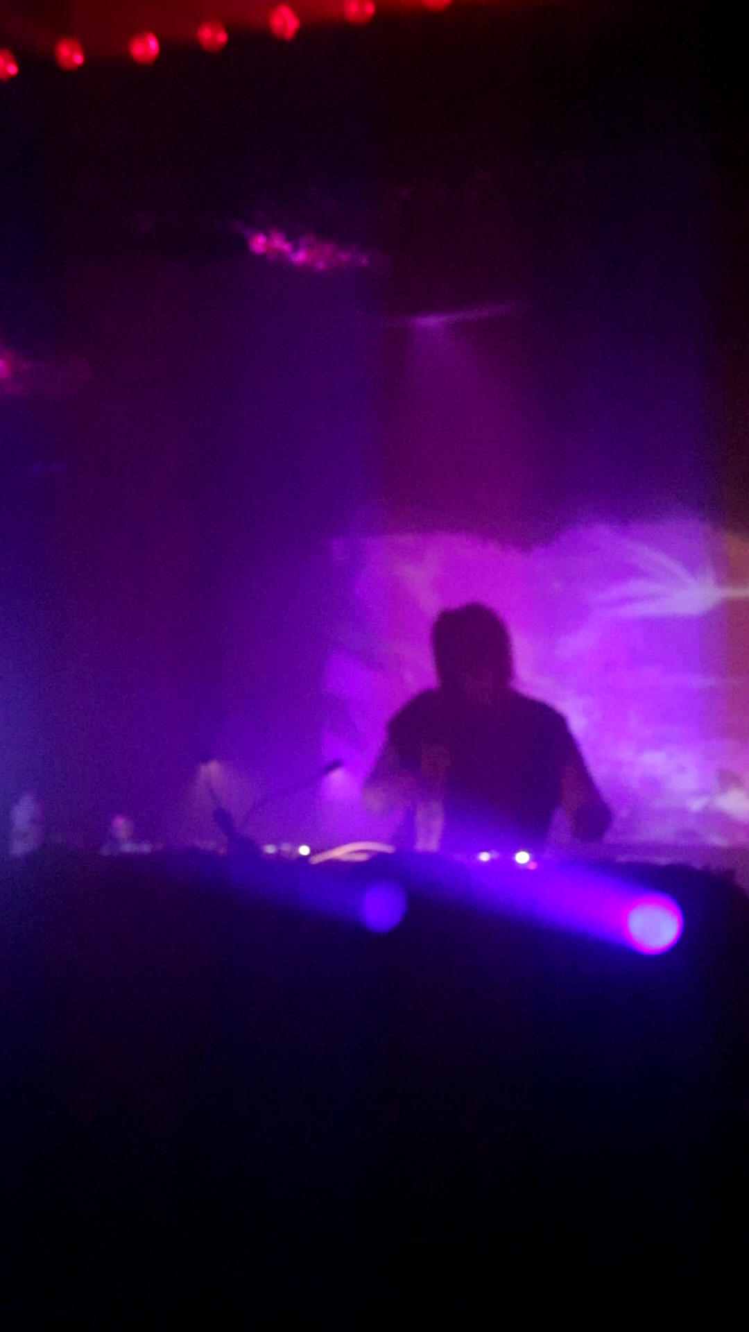Grainy low resolution photo of DJ wearing Tshirt with sleeves cut off performing in silhoutte from video projection behind decks. emo samurai vibes.