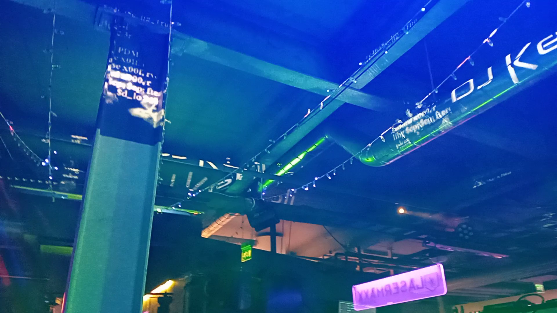 Industrial pillars and pipes at a venue with dark code, glowing, and DJ logo projection mapped onto them